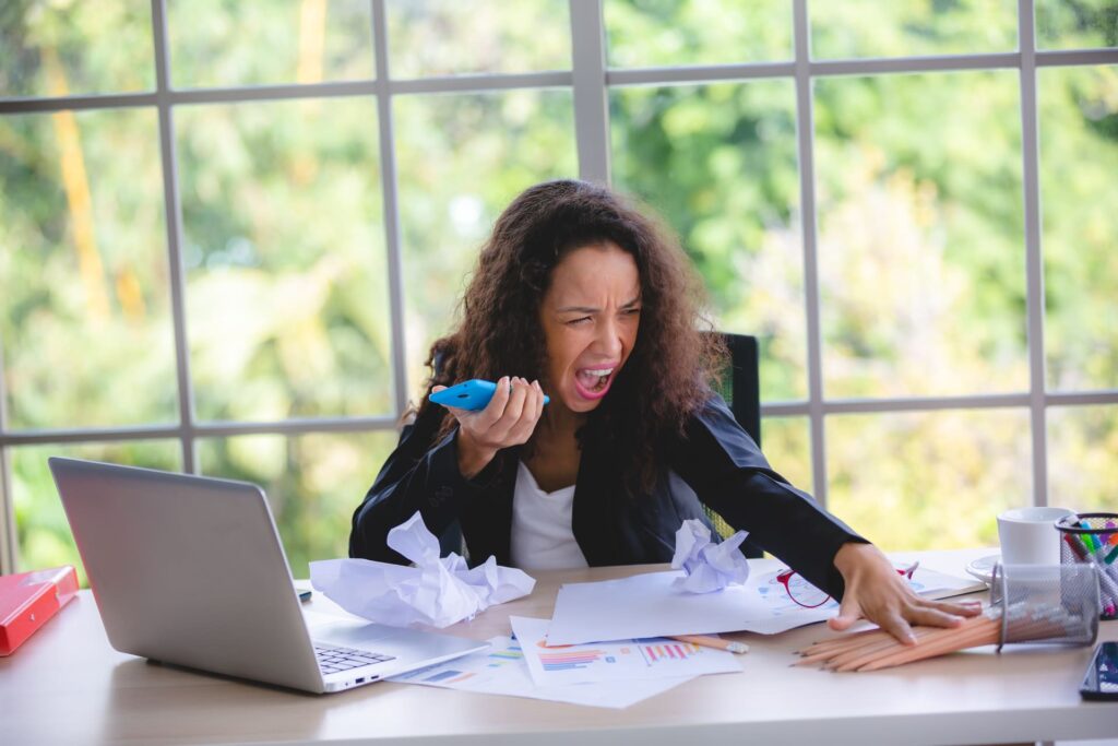 Vishing and Phishing - Frustrated-businesswoman-shouting-at-phone-in-messy-office