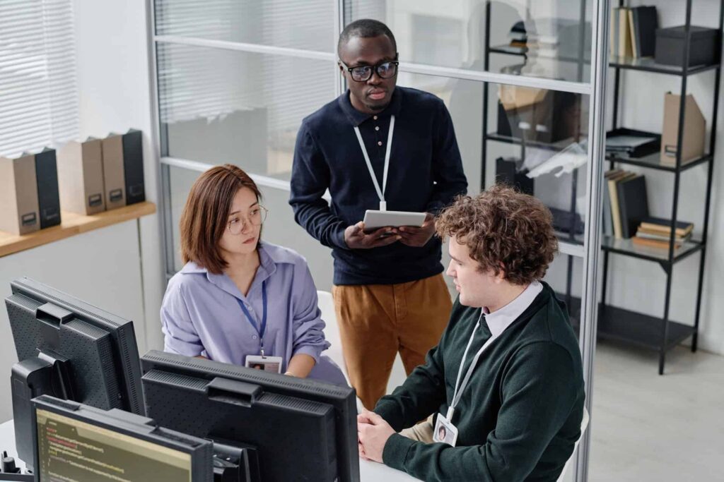 Small team discussing work at desks one person holding a tablet while others look at monitors - CMIT Solutions GDPR compliance guide for businesses in the US