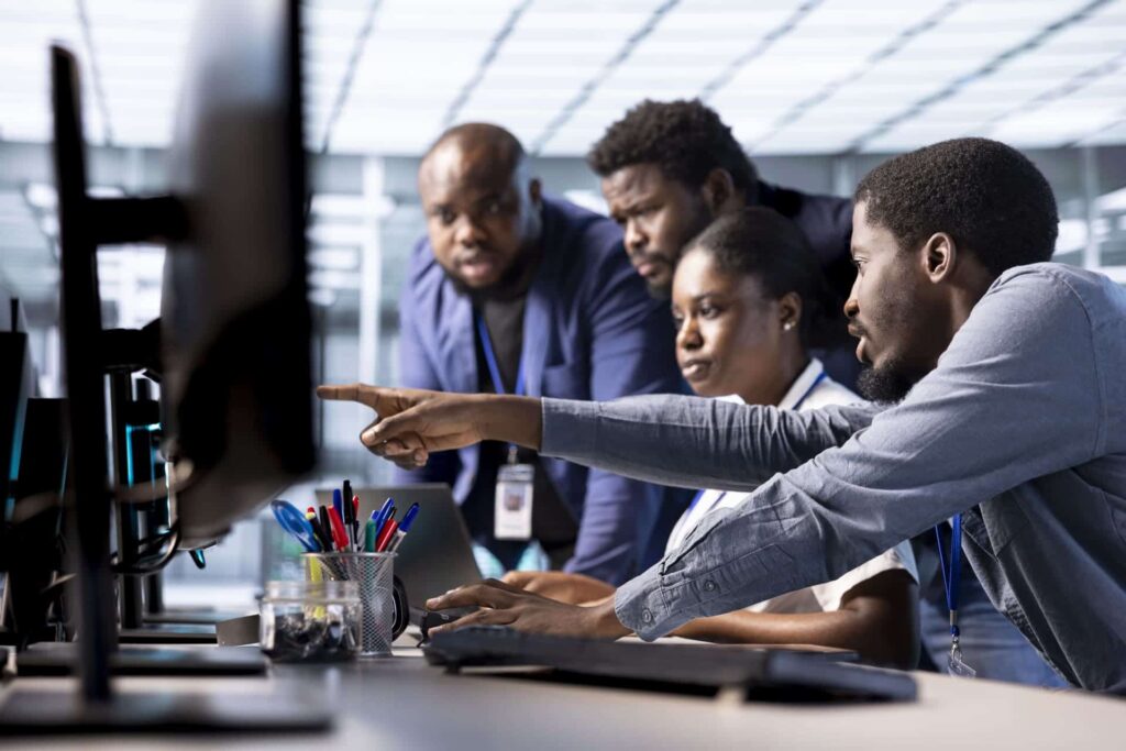 Team of four coworkers pointing at a computer screen while collaborating in an office - CMIT Solutions What Is PCI-DSS Compliance? Requirements, Checklist & More