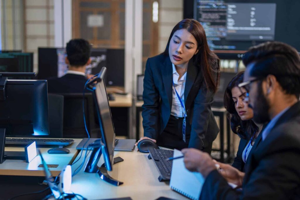 Three professionals reviewing code on computers one leaning in to assist teammates - CMIT Solutions What Is PCI-DSS Compliance? Requirements, Checklist & More